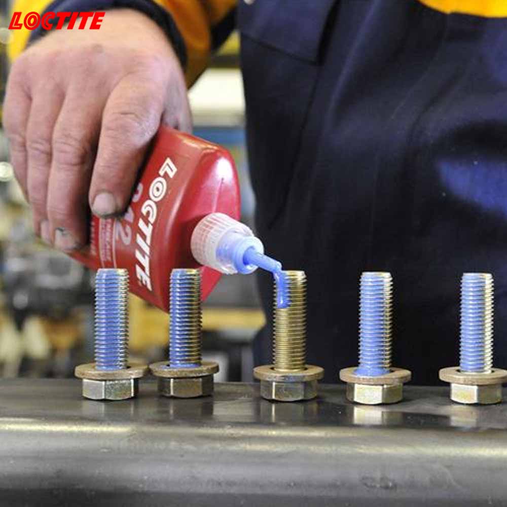 Person applying LOCTITE thread locker to screws on a workbench.