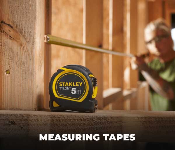 Stanley measuring tape on a wooden surface with a construction worker in the background.